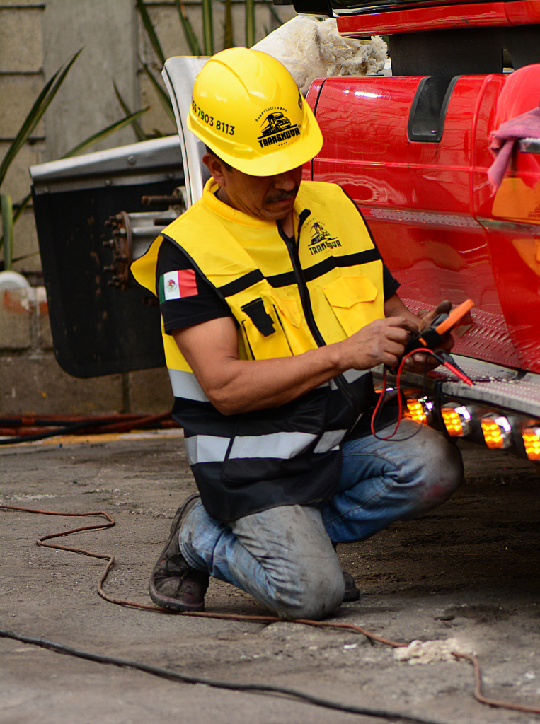 Técnico de transporte de carga pesada revisando el sistema eléctrico de un camión especializado.